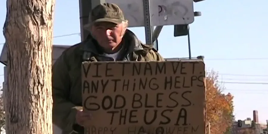 A man at a roadside holding a hand-lettered cardboard sign